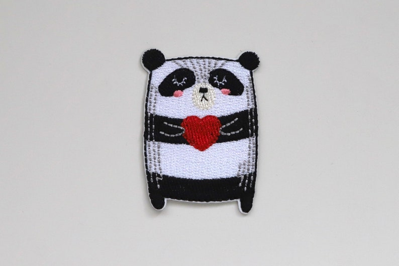 May include: Embroidered iron-on patch featuring a black and white panda holding a red heart. The panda has a cute, cartoon-like expression.