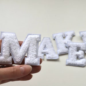 May include: White felt letters spelling out the word "MAKER". The letters are puffy and have a textured surface.