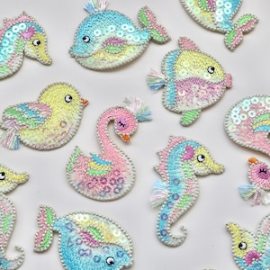 May include: Assortment of colourful, sequined, embroidered iron-on patches featuring various sea creatures and birds. The patches include a swan, a seahorse, a fish, a whale, and a bird.