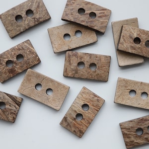 May include: A collection of 10 brown coconut shell buttons, each with two holes. The buttons are rectangular and have a natural, rustic look.