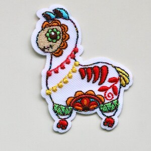 May include: Embroidered white alpaca patch with colourful Day of the Dead inspired details. The alpaca has a floral design on its head and body, with red, orange, yellow, green, and blue accents.