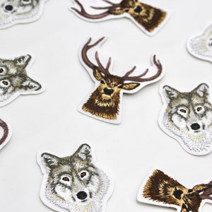 May include: Eight embroidered iron-on patches featuring animal heads. The patches include a deer, a wolf, and a fox. The patches are all in shades of brown, grey, and white.