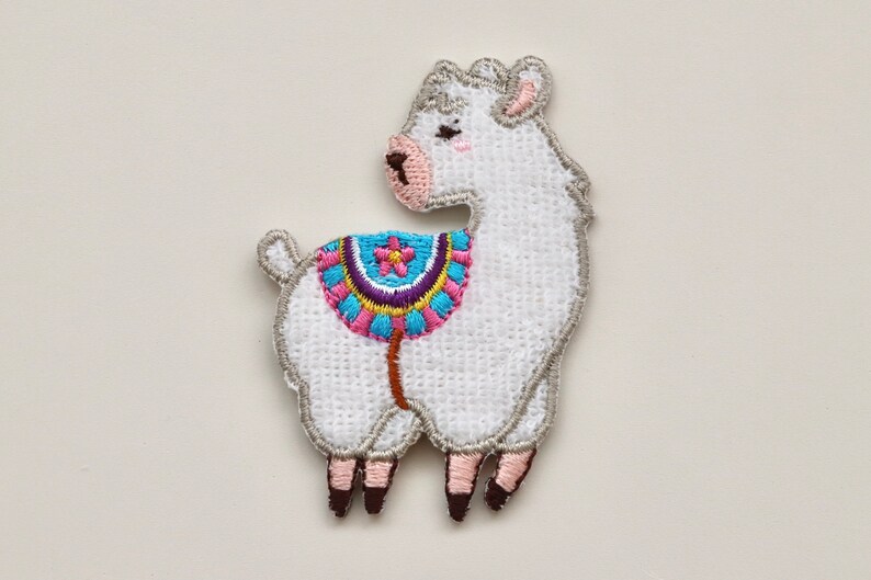 Puede incluir: Parche de llama blanco bordado con una silla de montar colorida. La llama est&aacute; de pie sobre cuatro patas y tiene la nariz y las orejas rosas.