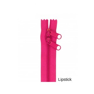 May include: A bright pink zipper with two metal sliders. The zipper is closed and the sliders are in the up position. The zipper is labeled "Lipstick".