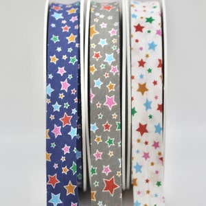 May include: Three spools of colourful fabric ribbon with a star pattern. The ribbon is blue, grey, and white with multi-coloured stars.