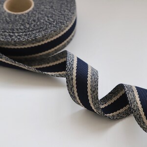 May include: A roll of navy blue and cream striped ribbon with a textured surface. The ribbon is rolled up and a portion is unfurled, showing the striped pattern.