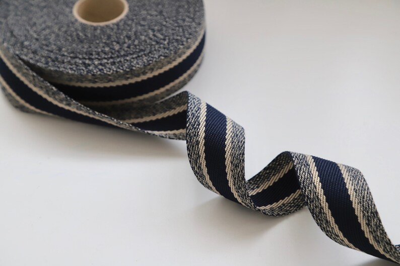 May include: A roll of navy blue and cream striped ribbon with a textured surface. The ribbon is rolled up and a portion is unfurled, showing the striped pattern.