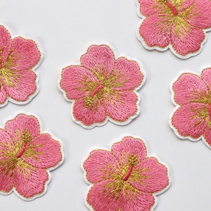 Puede incluir: Seis parches bordados de flores de hibisco rosas y doradas. Las flores tienen un contorno blanco y est&aacute;n sobre un fondo blanco.