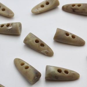 May include: A collection of twelve brown and white marbled plastic buttons, each with two holes. The buttons are shaped like a long oval with a pointed end.