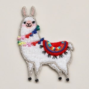 Puede incluir: Aplique de llama blanca bordada con una silla de montar y borlas de colores. La llama est&aacute; de pie sobre sus cuatro patas y tiene una cara amigable.