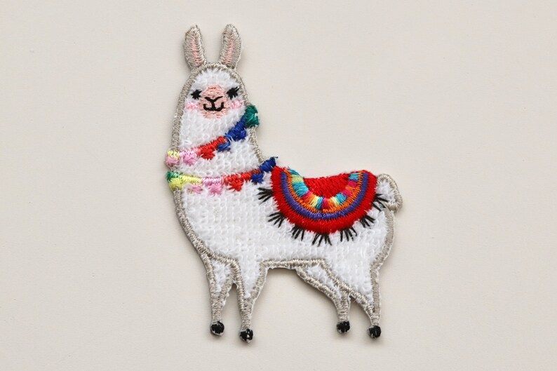 Puede incluir: Aplique de llama blanca bordada con una silla de montar y borlas de colores. La llama est&aacute; de pie sobre sus cuatro patas y tiene una cara amigable.