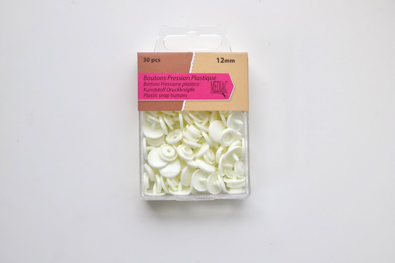 K&ouml;nnte beinhalten: Eine Packung mit 30 wei&szlig;en Kunststoff-Druckkn&ouml;pfen, 12 mm gro&szlig;. Die Verpackung ist mit "Boutons Pression Plastique" und "Mediac" beschriftet.