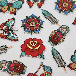 May include: Assortment of colourful embroidered iron-on patches featuring butterflies, flowers, cherries, feathers, and Russian nesting dolls.