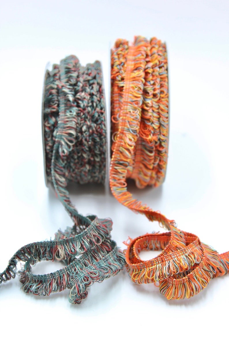 May include: Two spools of colorful trim with a fringed edge. One spool is teal and orange, the other is orange and yellow.