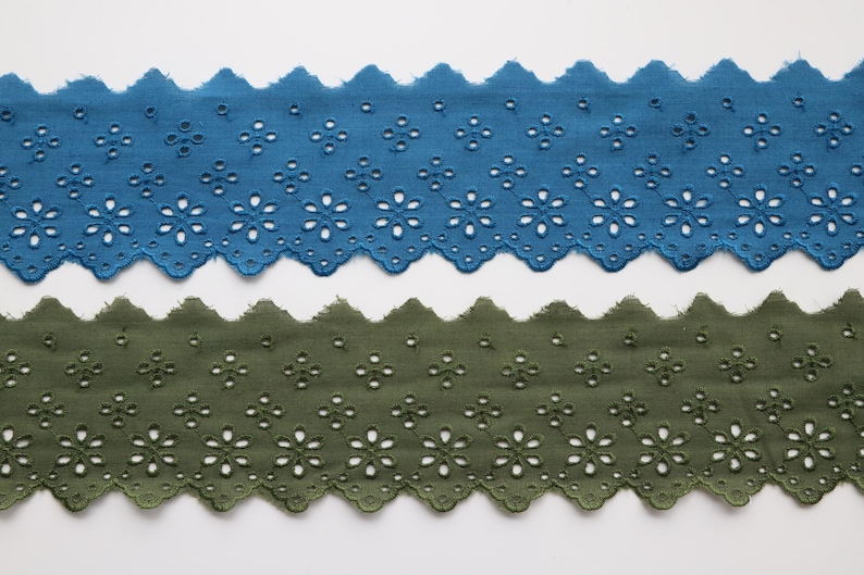 May include: Two pieces of scalloped cotton lace trim with a floral pattern. The top piece is teal blue and the bottom piece is olive green.