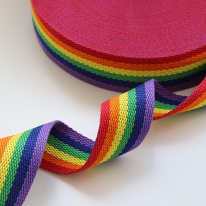 May include: Rainbow striped webbing, a type of flat woven strap, in red, orange, yellow, green, blue, indigo, and violet. The webbing is rolled up and a section is unfurled, showing the colors.