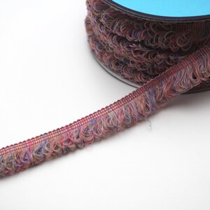 May include: A spool of multi-colored fringe trim with a blue plastic spool. The fringe is a mix of pink, blue, and beige.