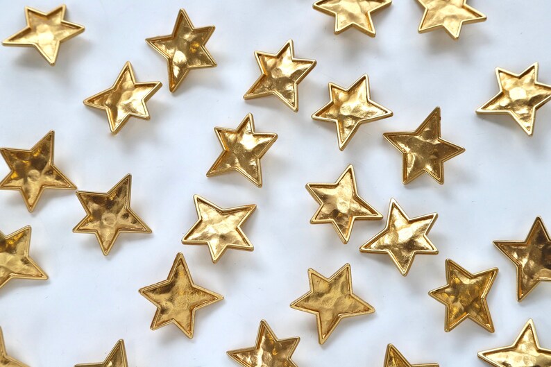 Puede incluir: Una colecci&oacute;n de adornos en forma de estrella de metal dorado esparcidos sobre un fondo blanco.