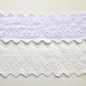 May include: Two pieces of white cotton eyelet lace trim with a scalloped edge and a floral pattern.