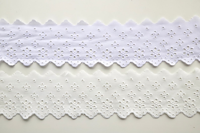 May include: Two pieces of white cotton eyelet lace trim with a scalloped edge and a floral pattern.
