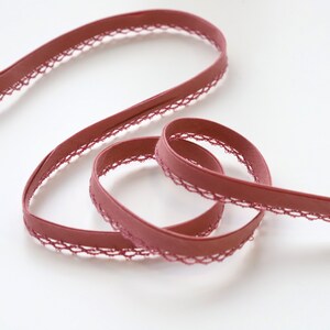 May include: A close-up of a maroon elastic trim with a delicate lace edge. The trim is soft and flexible, making it ideal for sewing projects.
