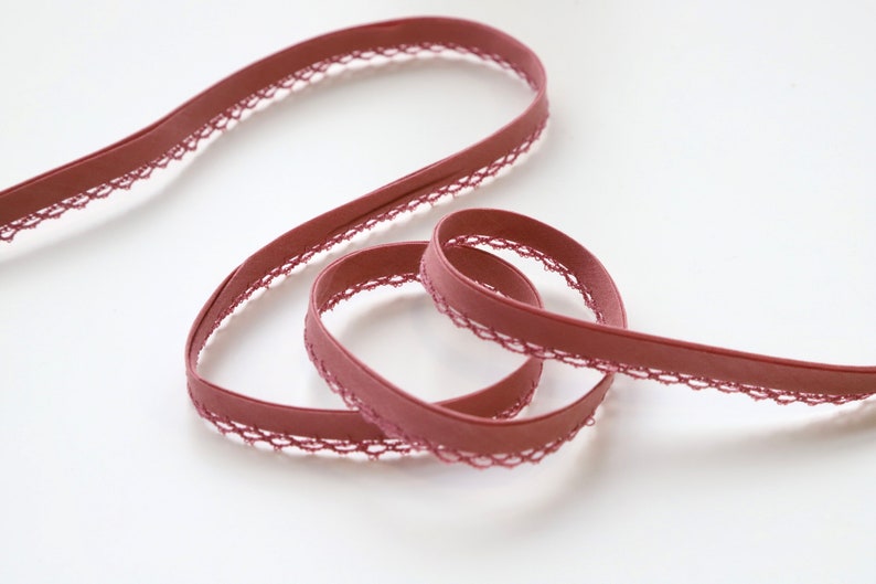 May include: A close-up of a maroon elastic trim with a delicate lace edge. The trim is soft and flexible, making it ideal for sewing projects.