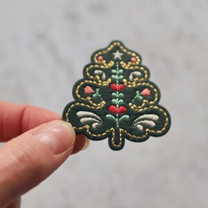 Peut inclure: Un patch de sapin de No&euml;l en feutre vert avec des broderies dor&eacute;es, blanches et roses. L'arbre est d&eacute;cor&eacute; d'une &eacute;toile, de c&oelig;urs et de fleurs.