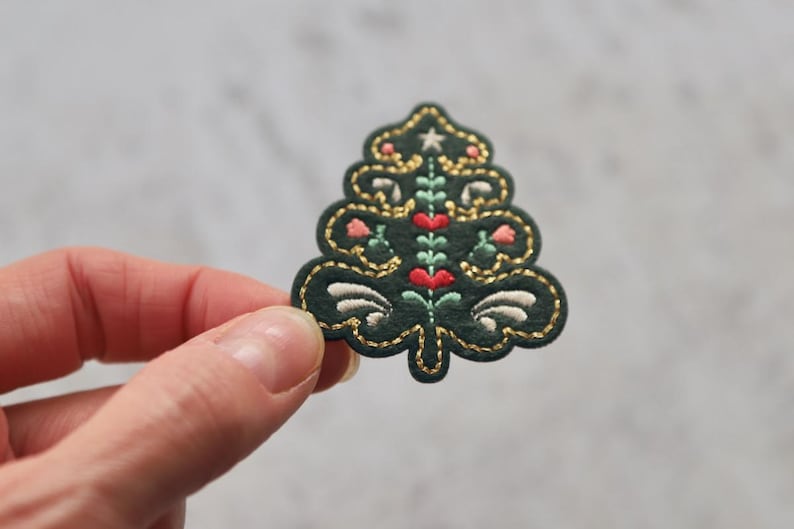 Peut inclure: Un patch de sapin de No&euml;l en feutre vert avec des broderies dor&eacute;es, blanches et roses. L'arbre est d&eacute;cor&eacute; d'une &eacute;toile, de c&oelig;urs et de fleurs.