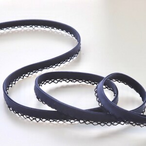 May include: A navy blue elastic trim with a black lace edging. The trim is folded and coiled on a white surface.