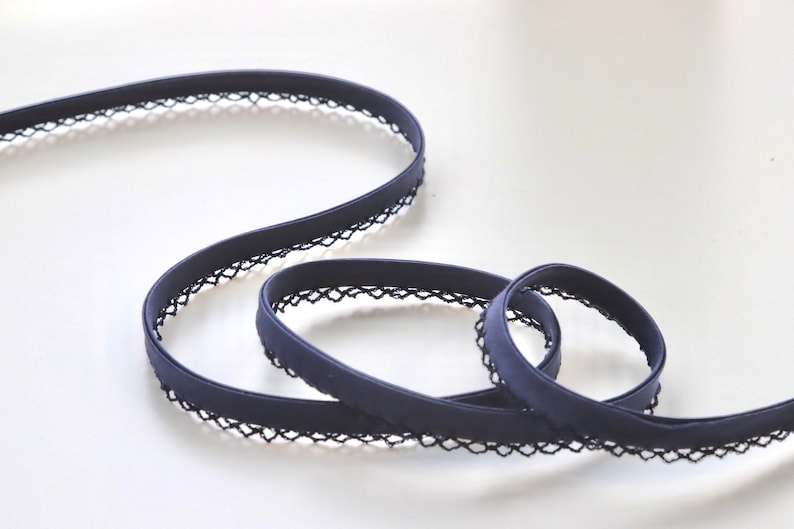 May include: A navy blue elastic trim with a black lace edging. The trim is folded and coiled on a white surface.