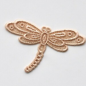 May include: A delicate, beige lace dragonfly applique. This intricate design features a detailed body and wings, perfect for adding a touch of whimsy to crafts and projects.