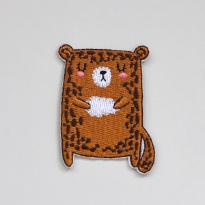May include: Brown embroidered iron-on patch of a cartoon bear with a white belly and closed eyes. The bear has a brown and black leopard print pattern.