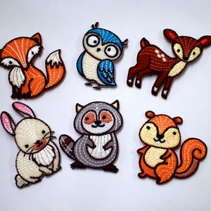 May include: Six embroidered iron-on patches featuring woodland animals: a fox, an owl, a deer, a rabbit, a raccoon, and a squirrel. The patches are colourful and detailed, with a whimsical style.