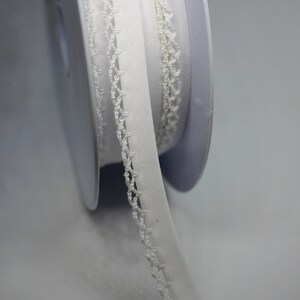 May include: White elastic trim with a delicate crocheted edge. The trim is rolled up on a spool.