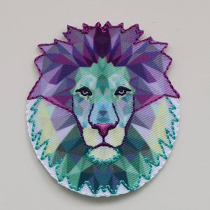 May include: A colorful geometric lion head patch with a purple, green, and blue color scheme. The patch is embroidered with a white outline.