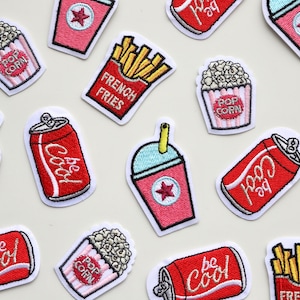 May include: A set of 11 embroidered iron-on patches featuring various cinema snacks and drinks. The patches include popcorn, french fries, soda, and slushies. The patches are all red, white, and blue.