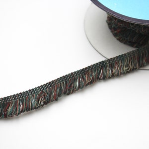 May include: A spool of green, brown, and gold trim with a fringed edge. The trim is approximately 1/2 inch wide.
