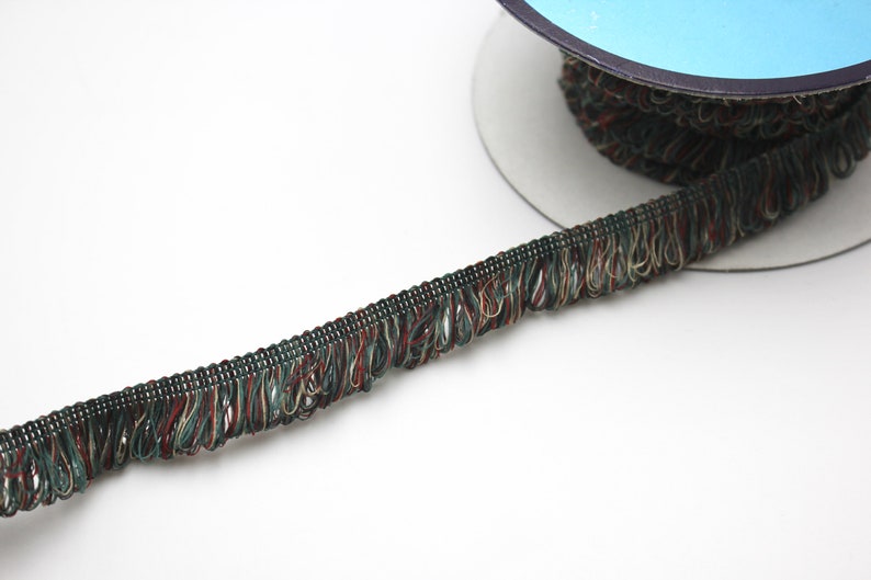 May include: A spool of green, brown, and gold trim with a fringed edge. The trim is approximately 1/2 inch wide.