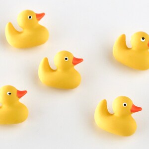 May include: Five yellow rubber duck toys with orange beaks and small black eyes are scattered on a white surface. The ducks are a classic bath toy, and are a cheerful addition to any collection.