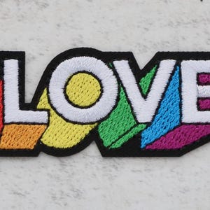 May include: An embroidered patch with the word "LOVE" in white lettering, featuring a rainbow colour scheme.