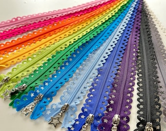 May include: A rainbow assortment of zipper tape with a star-shaped cut-out design. The zipper tape is arranged in a fan shape, with the colours ranging from pink to black.