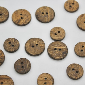 May include: A collection of brown coconut shell buttons with two holes each. The buttons are arranged on a white surface.
