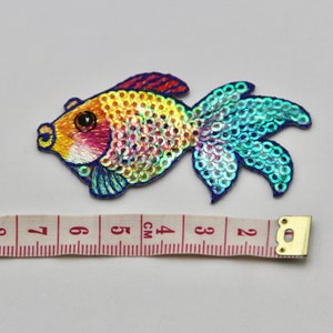 May include: A colorful iridescent fish-shaped sequin patch with blue, green, yellow, orange, and pink sequins. The patch is about 4 cm long and is perfect for adding a touch of whimsy to clothing or crafts.