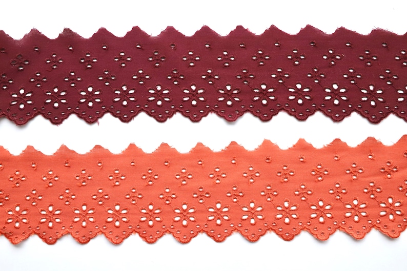May include: Two pieces of brown and orange cotton lace trim with a scalloped edge and a floral pattern.