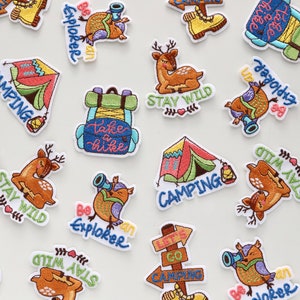 May include: A collection of colourful embroidered iron-on patches featuring camping and nature themes. The patches include images of tents, backpacks, deer, owls, and a sign that says "Let's Go Camping".