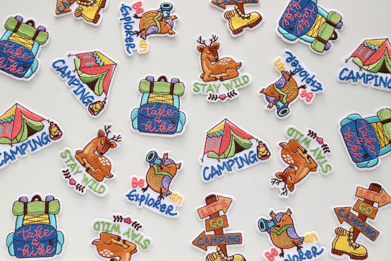 May include: A collection of colorful embroidered iron-on patches featuring camping and nature themes. The patches include images of tents, backpacks, deer, owls, and a sign that says "Let's Go Camping".