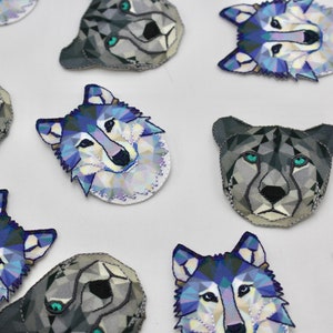 May include: A collection of 10 colourful geometric wolf and cheetah face patches. The patches are made of fabric and have a white background with blue, purple, and grey geometric shapes.