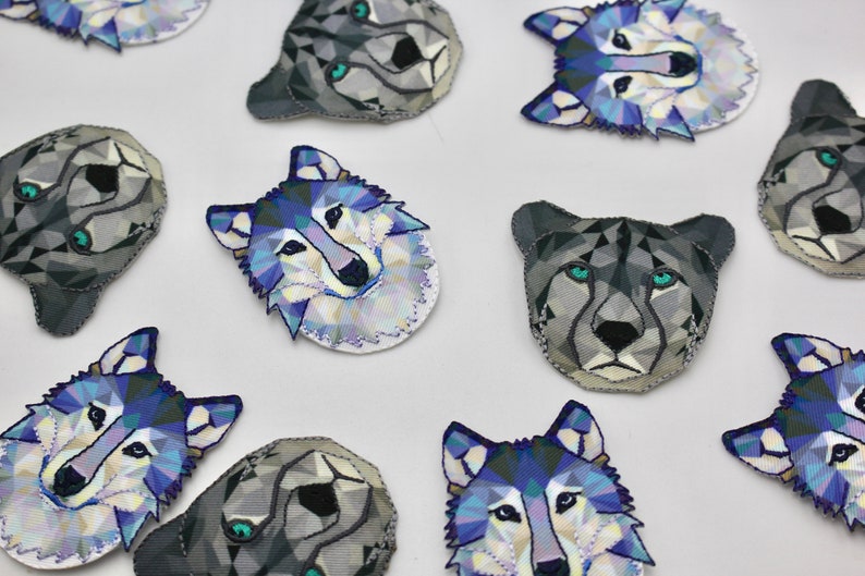 May include: A collection of 10 colorful geometric wolf and cheetah face patches. The patches are made of fabric and have a white background with blue, purple, and gray geometric shapes.