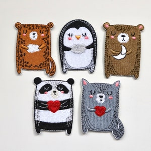 May include: Five embroidered iron-on patches featuring cute animal designs. The patches include a brown bear holding a moon, a penguin, a brown bear holding a heart, a panda holding a heart, and a grey cat holding a heart.