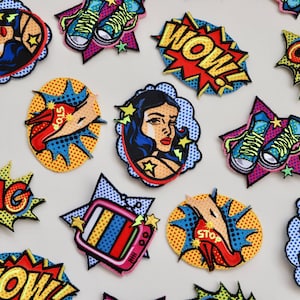 May include: A collection of colourful iron-on patches featuring pop art style designs. The patches include images of a woman, shoes, a television, and words like "WOW!" and "OMG!"